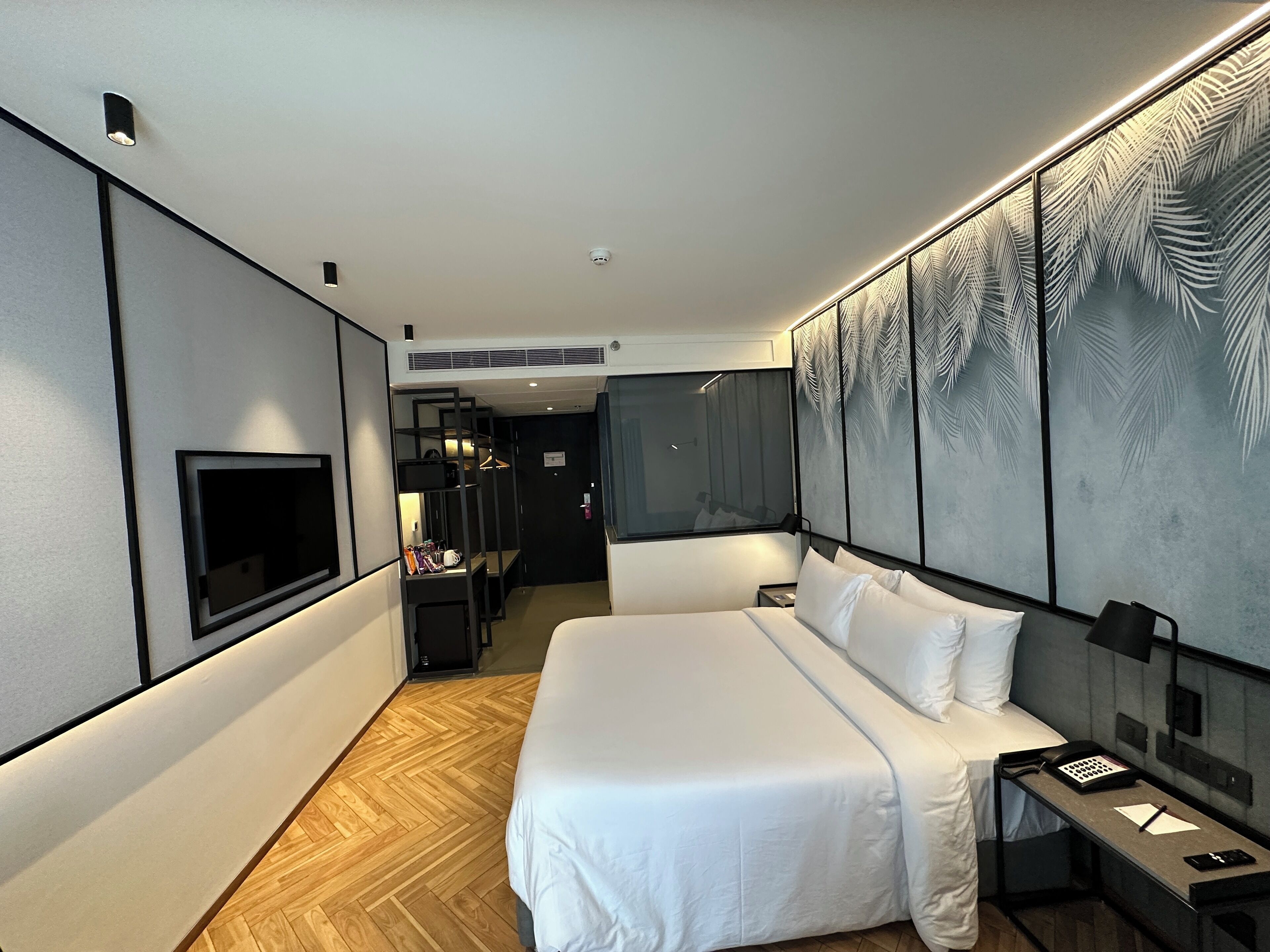 A modern hotel room with a large bed, a TV mounted on the wall, a desk with a phone, and a decorative wall panel.