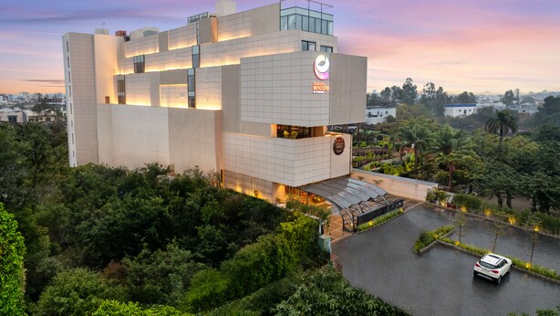 A modern building with a prominent logo, surrounded by lush greenery and a parking area. - Ramada Encore By Wyndham Ambala Gt Road (Ambala)