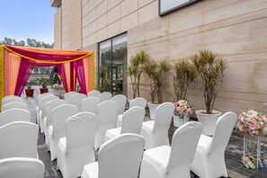 Allestimento cerimonia nuziale con sedie bianche e una tenda drappeggiata in rosso e arancione.