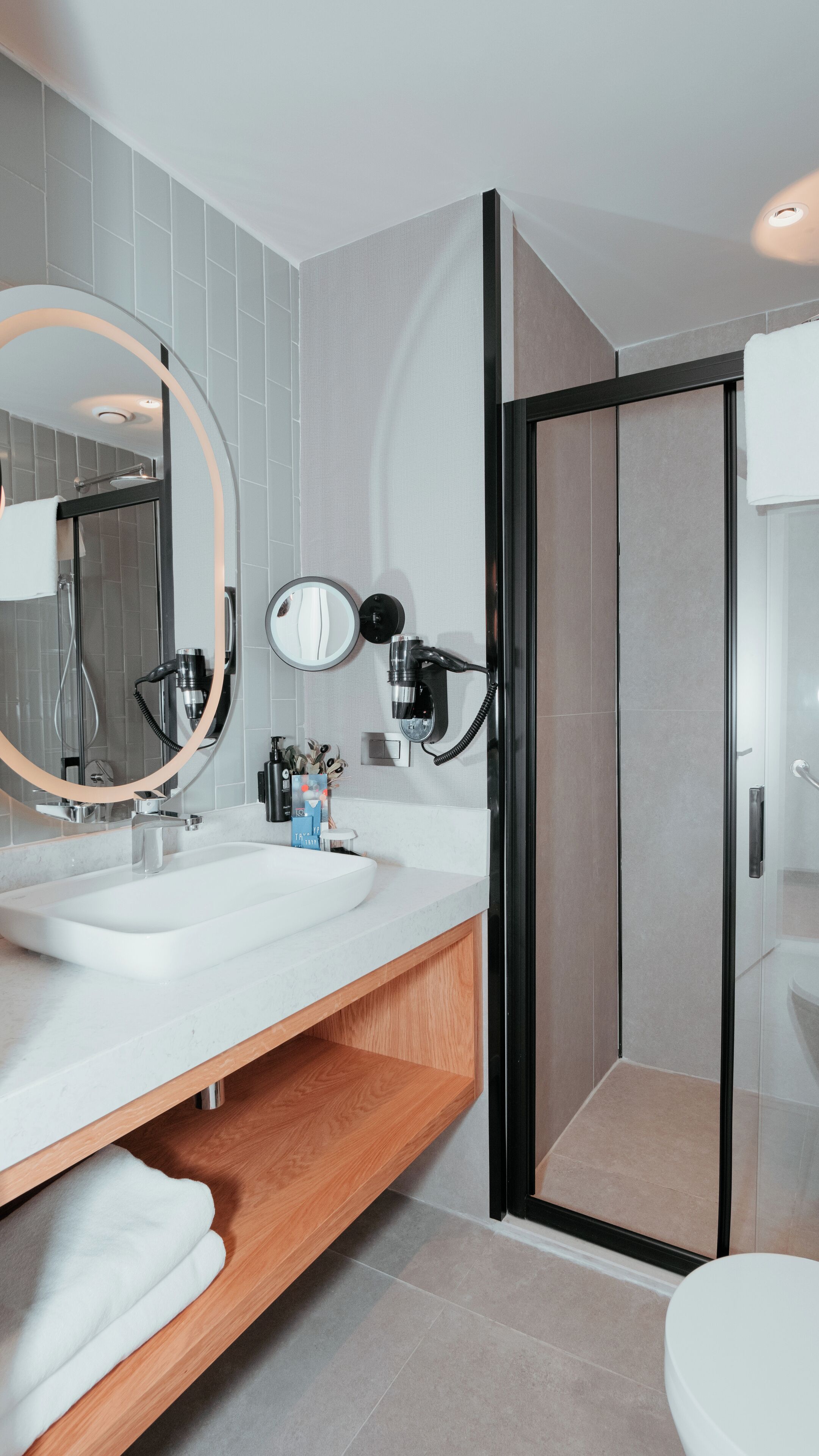 A modern bathroom with a large mirror, two sinks, a shower, and a toilet.