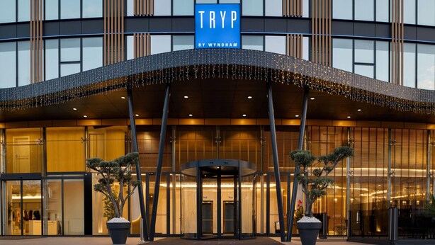 Une entrée d’hôtel moderne avec une porte tournante, de grandes fenêtres et une enseigne indiquant « TRYP BY WYNDHAM ».
