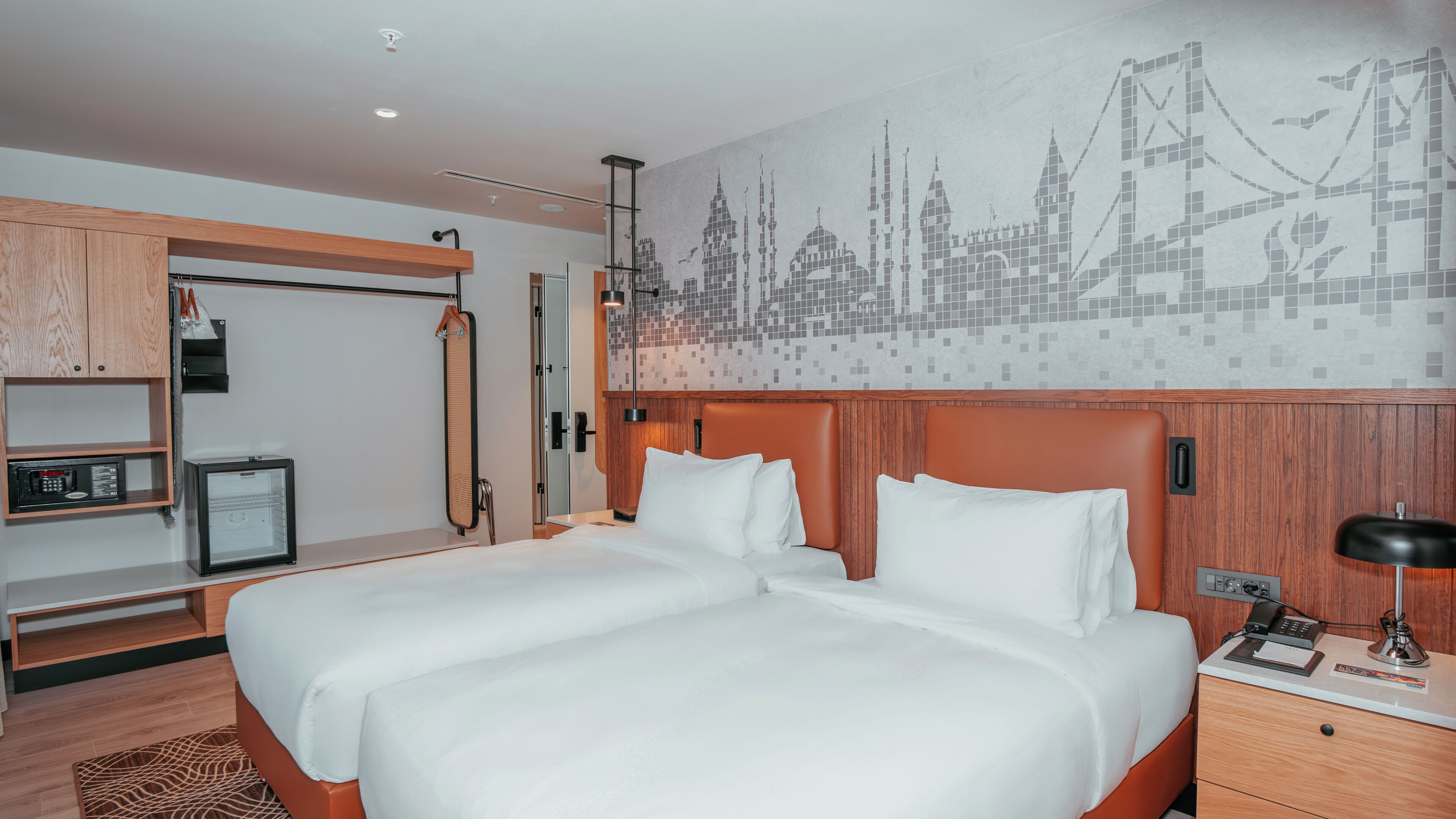 Ein Hotelzimmer mit einem großen Bett, einer Minibar, einem Kleiderhaken und einem Wandbild.