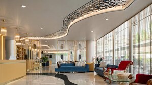 Un hall d’entrée spacieux avec un plafond incurvé, un canapé bleu, un fauteuil rouge et une table basse en verre.