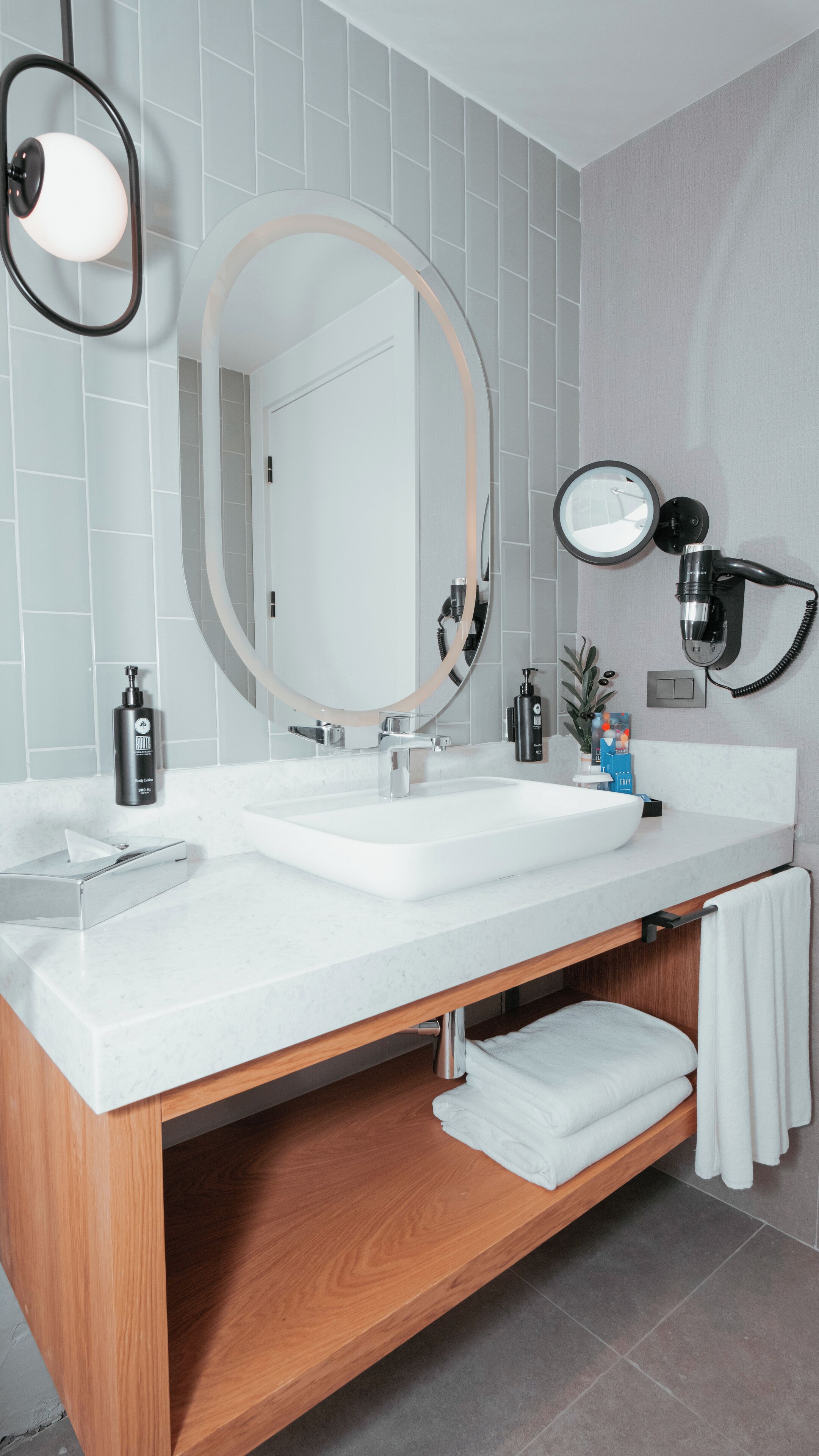 A modern bathroom with a white sink, a large mirror, and a towel rack.