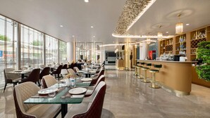 Un espace repas moderne avec des tables en verre, des chaises rembourrées et un bar avec des tabourets.