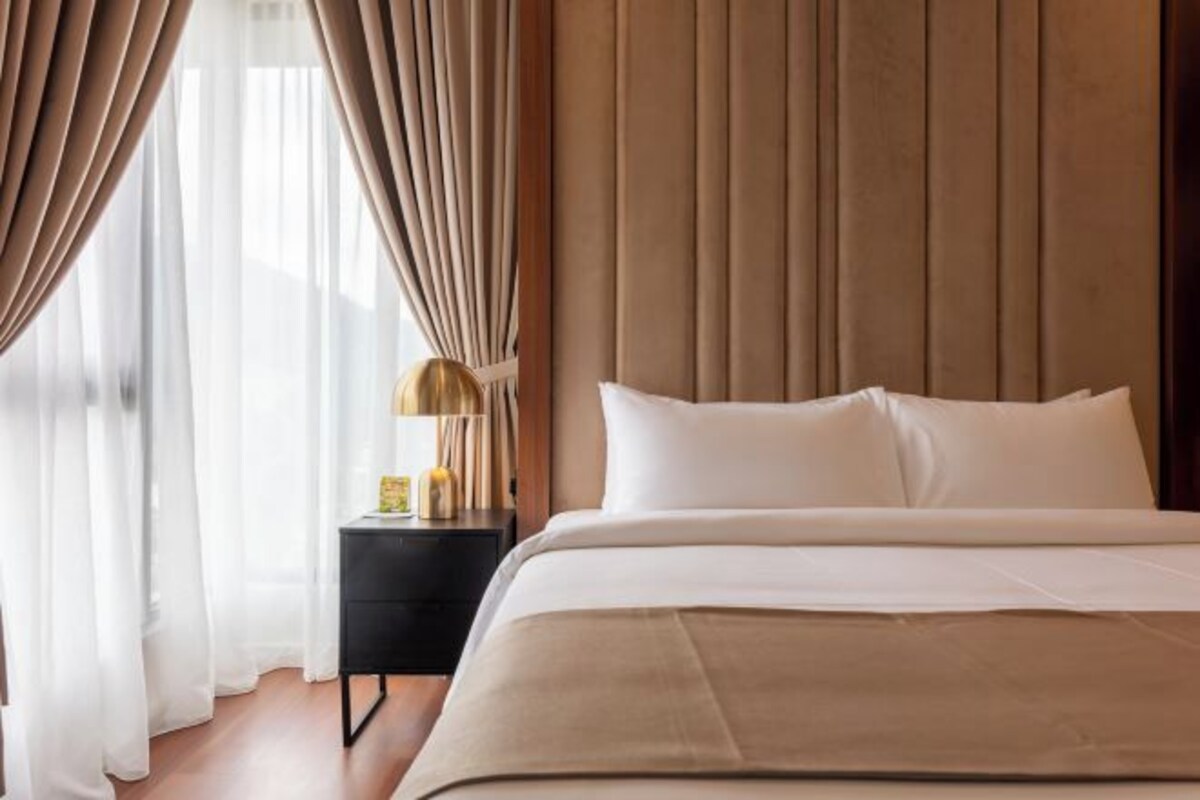 Une chambre d’hôtel avec un lit, des rideaux, une table de chevet et une lampe.