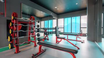 A modern gym with weightlifting equipment, a bench, and large windows offering a view of the outdoors.