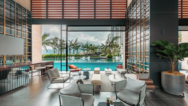 Un área de descanso al aire libre moderna con piscina, asientos y vistas a palmeras y edificios.