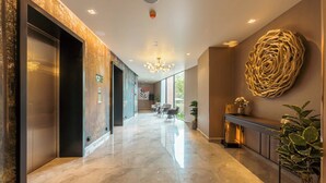 Un moderno vestíbulo de hotel con suelo de mármol, ascensores, un mostrador de recepción y una gran pieza decorativa en la pared.