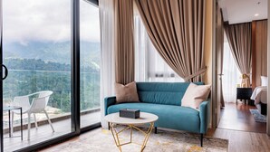 Una habitación de hotel moderna con un ventanal grande, un sofá color turquesa, una mesa de centro redonda y vistas a un paisaje montañoso.