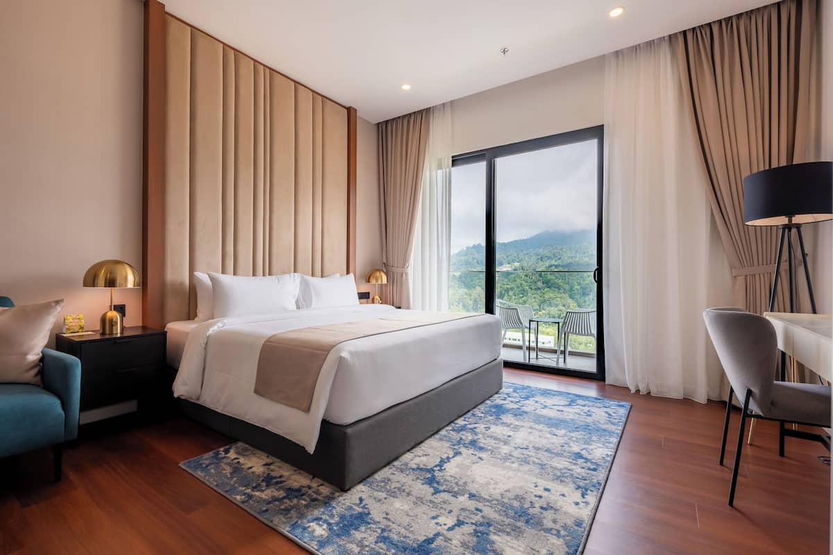 Habitación de hotel moderna con una cama grande, un escritorio, una silla y un balcón con vistas a las montañas.