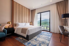 A modern hotel room with a large bed, a desk, a chair, and a balcony with a view of the mountains. - Wyndham Garden Suites Genting Highlands (Genting Highlands)