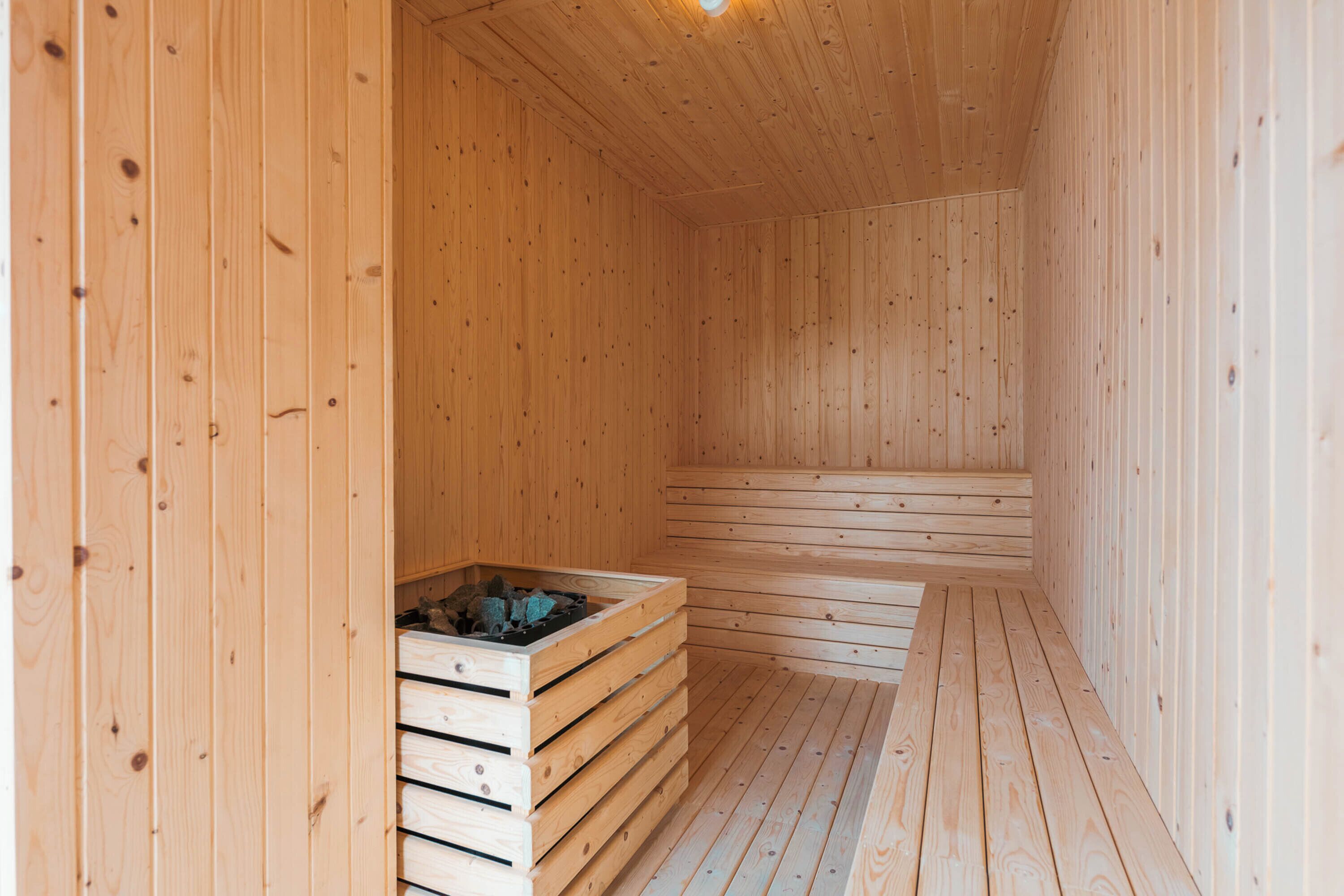 Una sauna in legno con panche e una vasca piena di pietre.