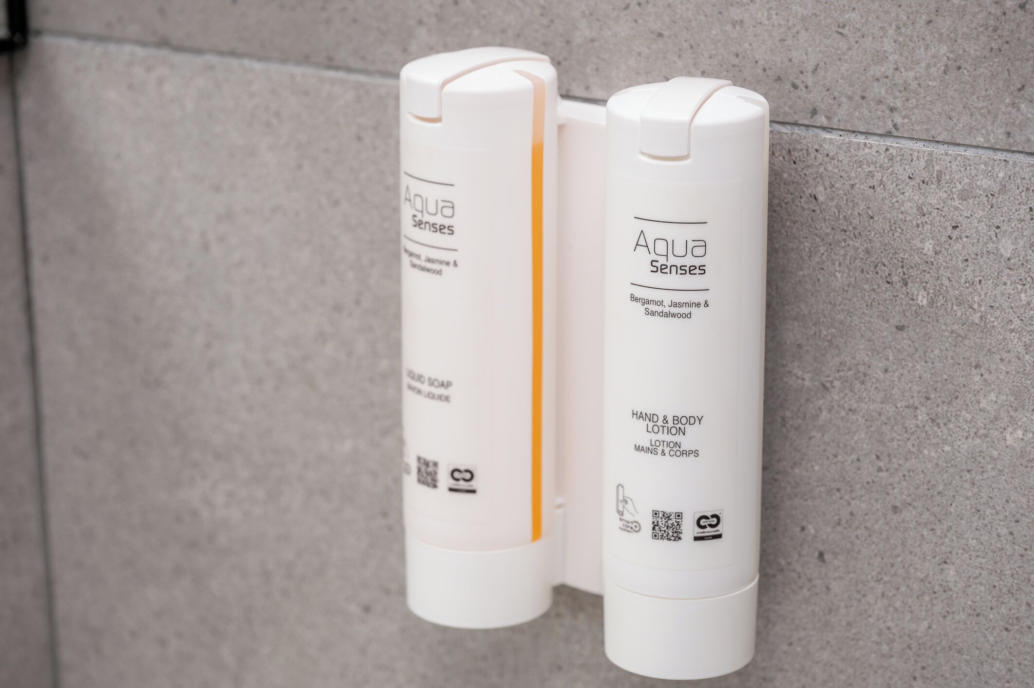 Two white bottles of Aqua Senses liquid soap and lotion against a textured wall.