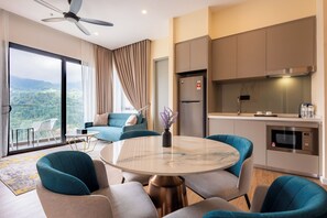 A modern hotel room with a balcony, a round marble table, teal chairs, a kitchenette, and a large window with a view of the mountains. - Wyndham Garden Suites Genting Highlands (Genting Highlands)