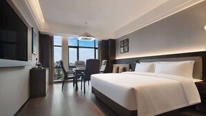 A modern hotel room with a large bed, a desk with a chair, a TV, and a view of the city through large windows. - Days Hotel By Wyndham Zhuzhou Shifeng (Zhuzhou)