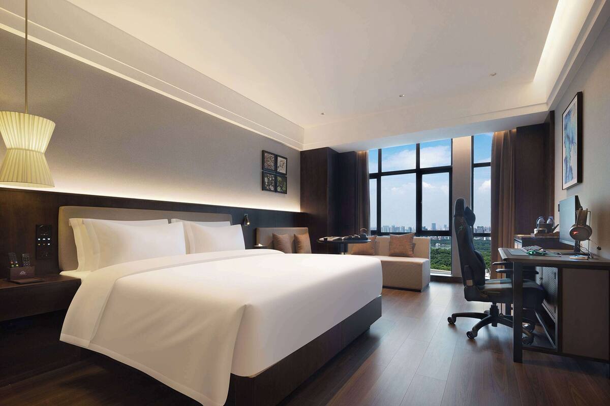 Ein modernes Hotelzimmer mit einem großen Bett, einem Schreibtisch und Blick auf die Stadt.