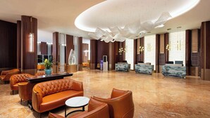 A spacious lobby with a modern design, featuring leather sofas, a marble reception desk, and a unique ceiling light fixture. - Ramada Plaza By Wyndham Wuhan Dongxi Lake (Wuhan)