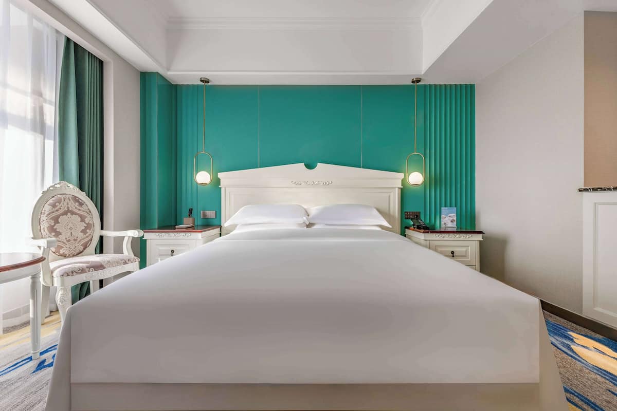 A large bed with a white headboard, two bedside tables with lamps, a chair, and teal walls.