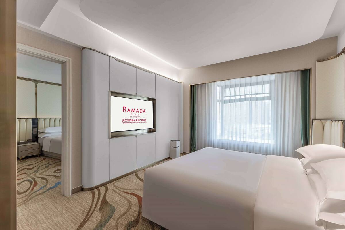 A modern hotel room with a large bed, a television mounted on the wall, and a window with curtains.