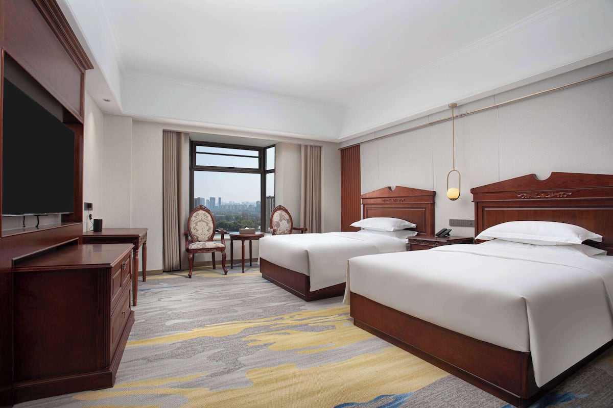 A hotel room with two beds, a desk, a chair, and a television.