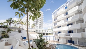 Un hotel moderno con zona de piscina, rodeado de palmeras y con varios balcones.