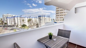 Un balcón con una mesa, sillas, una planta en maceta y vistas a edificios de apartamentos.