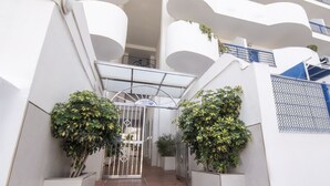 Un edificio moderno con paredes blancas y balcones. Dos macetas con plantas están en primer plano.