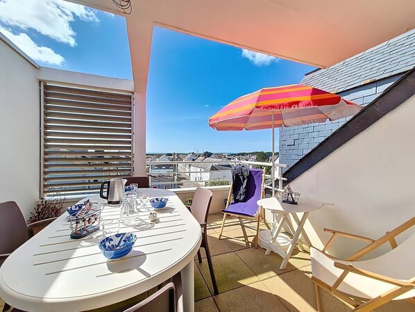 A balcony with a table set for two, a chair, a small table, and a colorful umbrella.