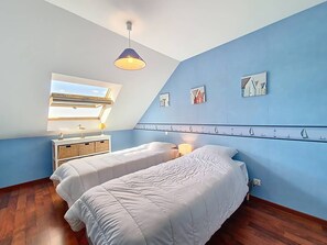 Ein Schlafzimmer mit zwei Betten, einem Oberlicht, einem Fenster, einem Nachttisch mit Lampe und Wandbildern.