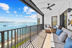 A balcony with a view of the sea, a sofa with patterned cushions, a ceiling fan, and a window with blinds. - Sweeping Gulf Views! (Naples)