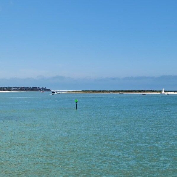 A coastal view with a clear sky, calm sea, and a distant shoreline with buildings and a sailboat. - Sweeping Gulf Views! (Naples)