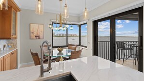 A kitchen with a large island, a dining area with a glass table, and a view of the ocean through large sliding doors.