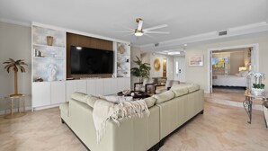 A spacious living room with a large sofa, a flat-screen TV, and a ceiling fan.