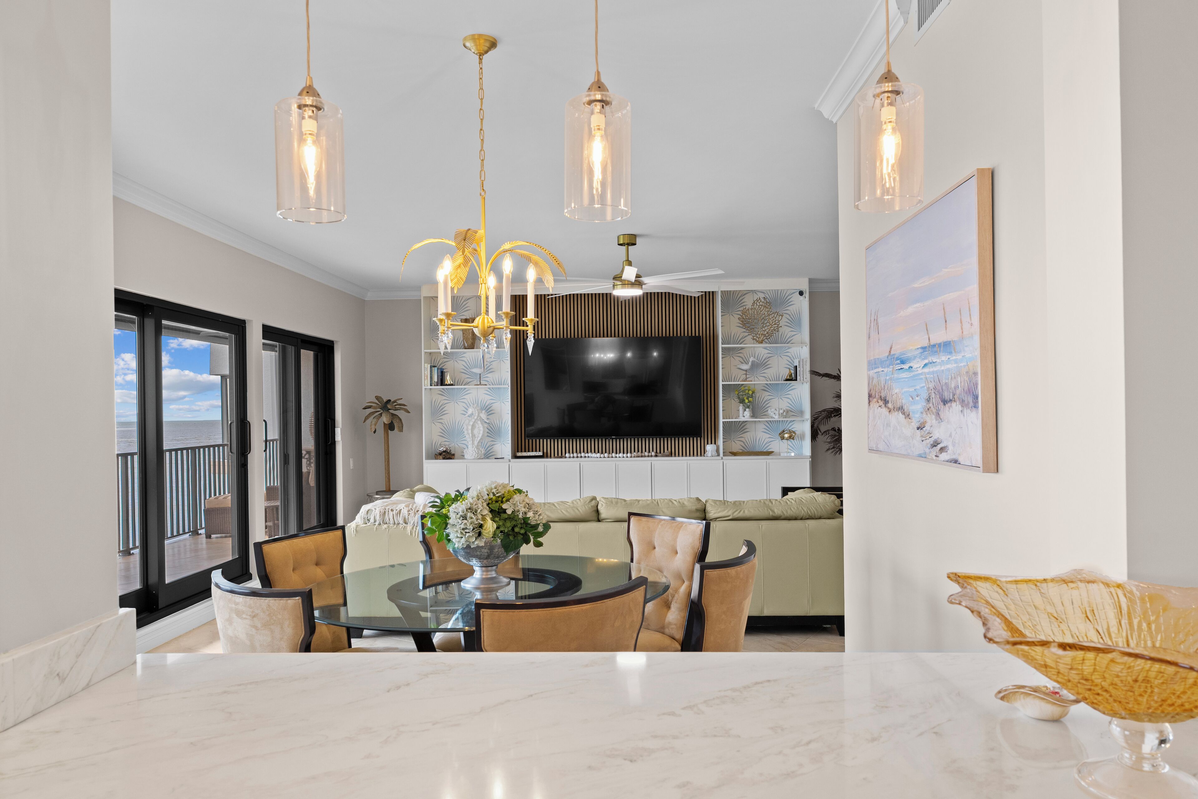 A modern living room with a glass dining table, comfortable seating, a large flat-screen TV, and decorative lighting.
