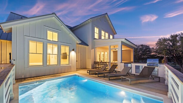 Une maison moderne dotée d’une piscine, d’un espace salon extérieur et d’un coin barbecue.