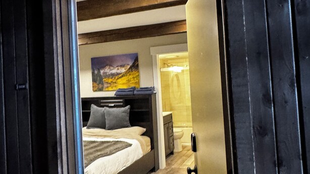 Une chambre à coucher avec un lit, une table de chevet, un tableau et une salle de bain visible à travers une porte ouverte.