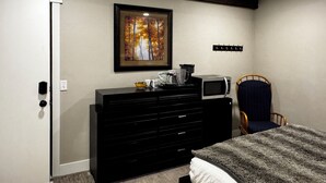 Une chambre à coucher avec un lit, une commode, une chaise, un four à micro-ondes et un tableau accroché au mur.