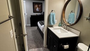 Une salle de bain avec un plancher en bois, des toilettes blanches, un meuble-lavabo avec un miroir et un espace douche.