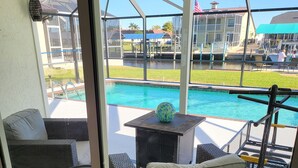 A glass-enclosed balcony with wicker furniture, a pool, and a view of a building with an American flag.