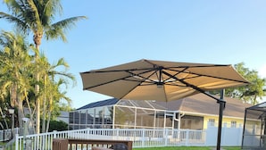 A patio area with a wooden deck, a covered seating area with a large umbrella, and a white fence surrounding the space.