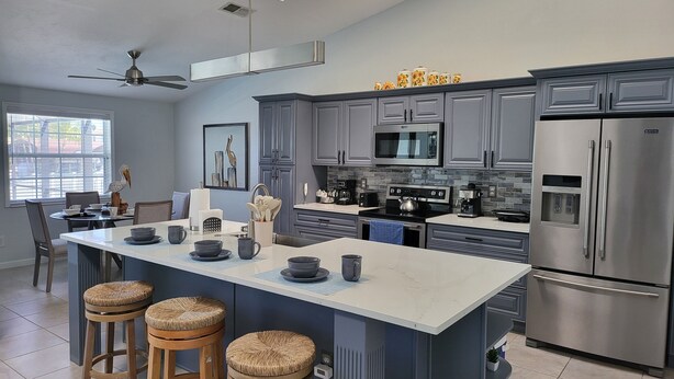 A modern kitchen with grey cabinets, a central island with stools, a microwave, a stove, and a refrigerator.