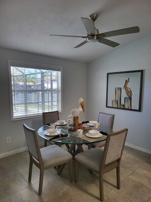 A dining area with a glass table, four chairs, a ceiling fan, a window with blinds, and a framed painting on the wall. - waterfront home, in a canal of the Caloosahatchee River with direct Gulf access. (Fort Myers)