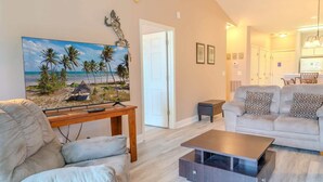 Een woonkamer met een strandthema schilderij, een bank, een salontafel en een eethoek met stoelen.