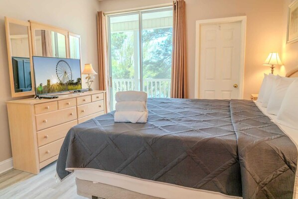 Um quarto com cama, cômoda, televisão e uma porta.