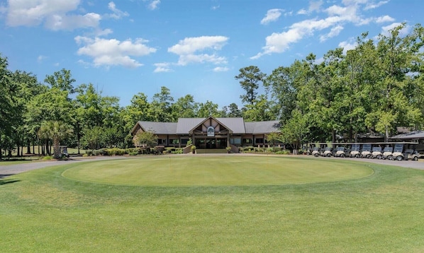 Ein Golfplatz mit Clubhaus, umgeben von Bäumen und Golfrollern.