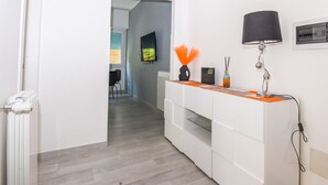 Un pasillo con una decoración en blanco y naranja, un radiador, un escritorio con una lámpara y un televisor en la pared.