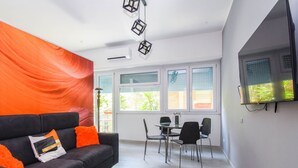 Una sala de estar moderna con un sofá negro, cortinas naranjas y una zona de comedor con mesa y sillas.