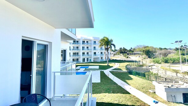 Ein modernes Gebäude mit Balkon, Pool und Blick auf andere Gebäude und Grünflächen.