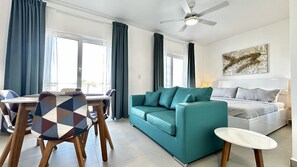 Una sala de estar moderna con un sofá color turquesa, un comedor con una mesa de diseño geométrico y un ventilador de techo.